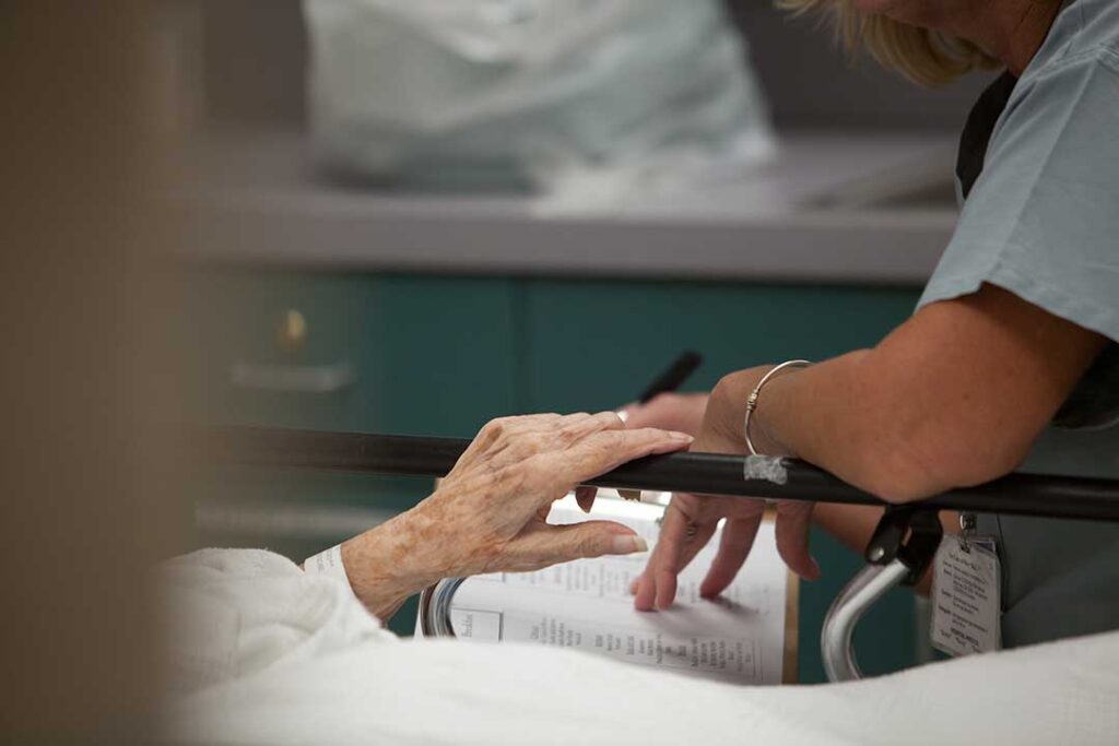 Volunteer talks with an older resident in a bright assisted living common room.